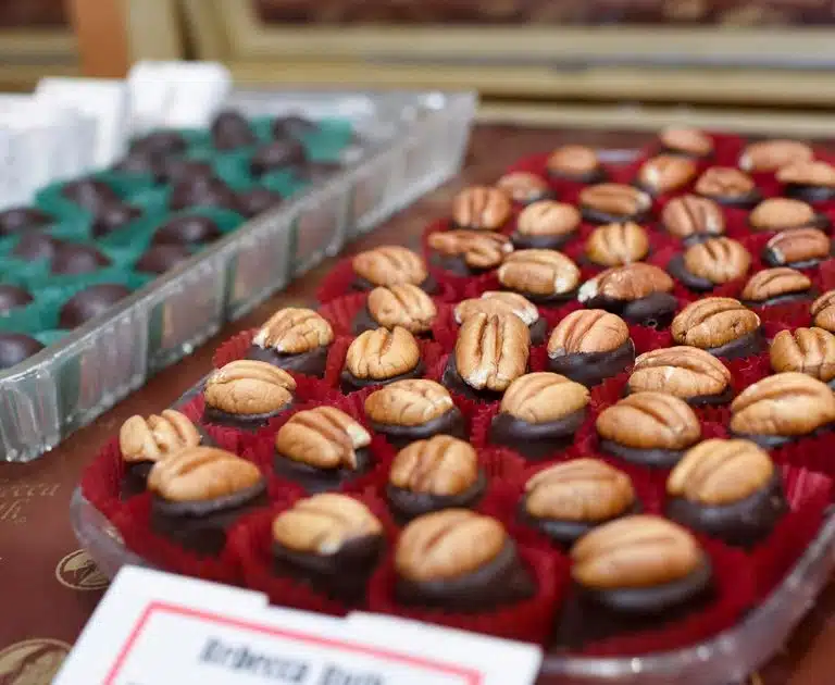 Tray of Bourbon Balls in a glass case. Bourbon Balls are a small, oval chocolate candy with a pecan on top.