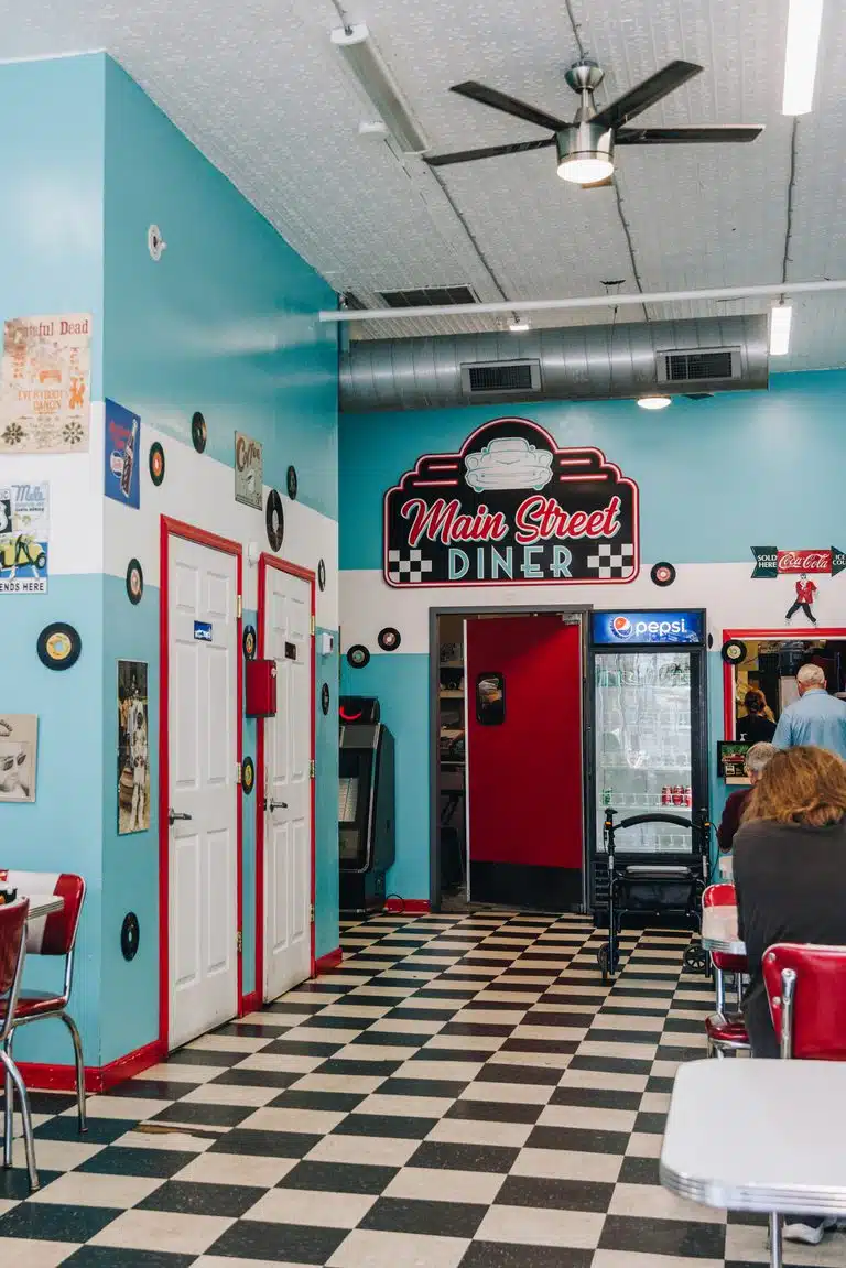 Cozy interior of Main Street Diner, showing a classic checkered floor, chrome and red vinyl chairs, and vintage 1950s memorabilia on the walls.