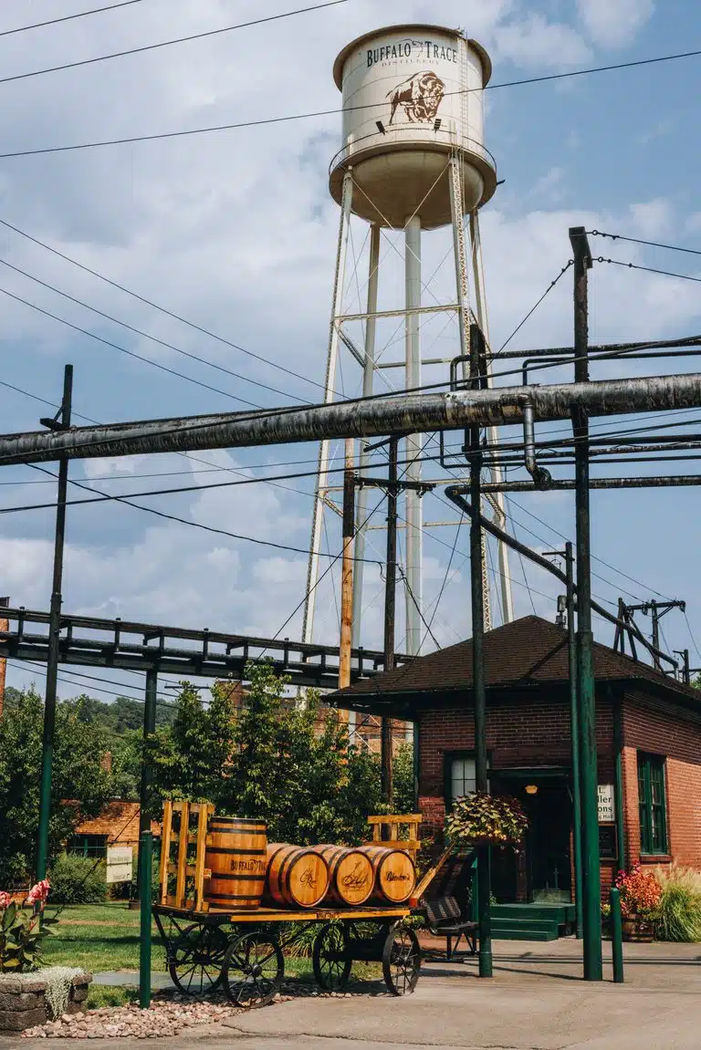 Brick building and iconic water tower looming over decorative wooden bourbon barrels displayed at Buffalo Trace Distillery's historic Frankfort campus.