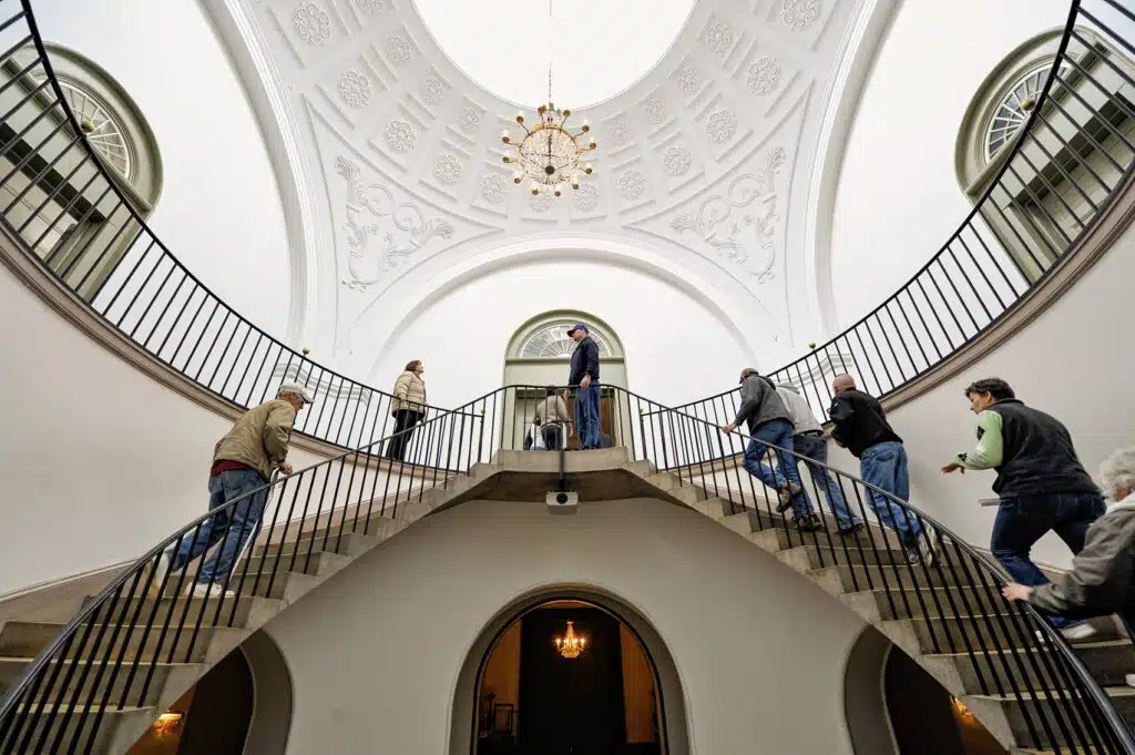Visitors walk up the double circular stone staircase inside the bright, white rotunda of Frankfort's historic Old State Capitol.