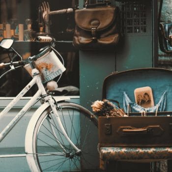 vintage bicycle parked outside storefront, accompanied by an open suitcase holding antique items