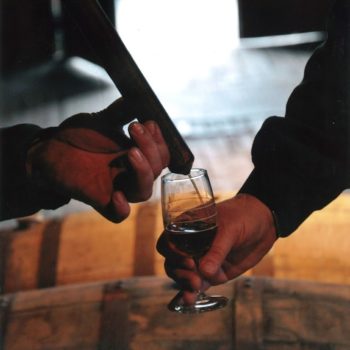 bourbon pouring in glass over barrels