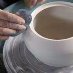 close up of a bowl on a potters wheel with a hand doing the finishing touches
