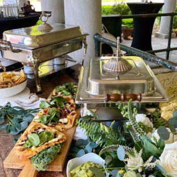 a catering set up with flower arrangements. There are flatbreads, guacamole, chips, and more.