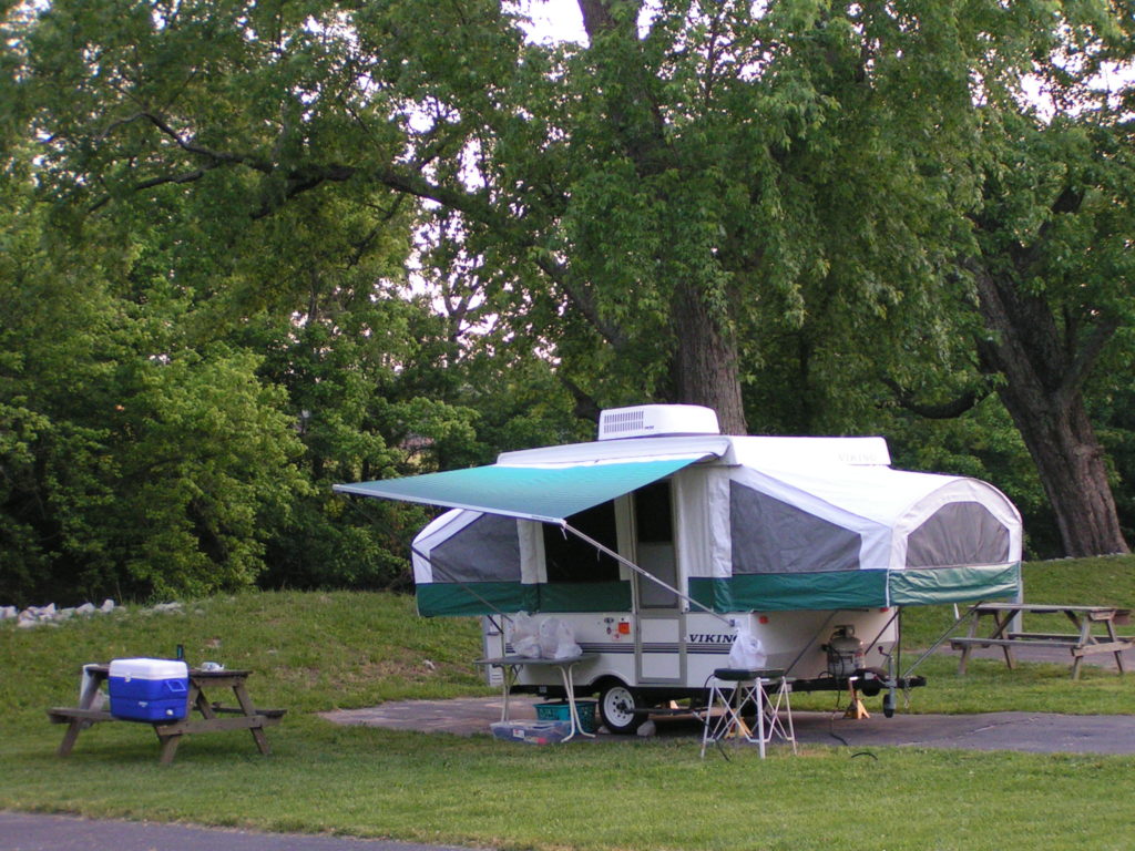 pop up camper set up in campground next to picnic table