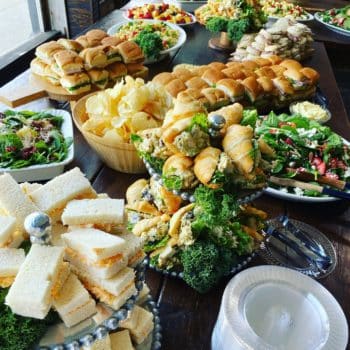 A spread of sandwiches, salads, chips, pasta salad, and fruit for catering at an event.