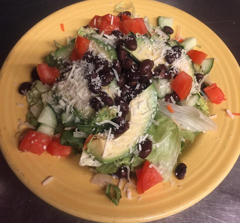 Yellow plate full of a Mexican dish containing rice, black beans, avocado, tomatoes, and peppers