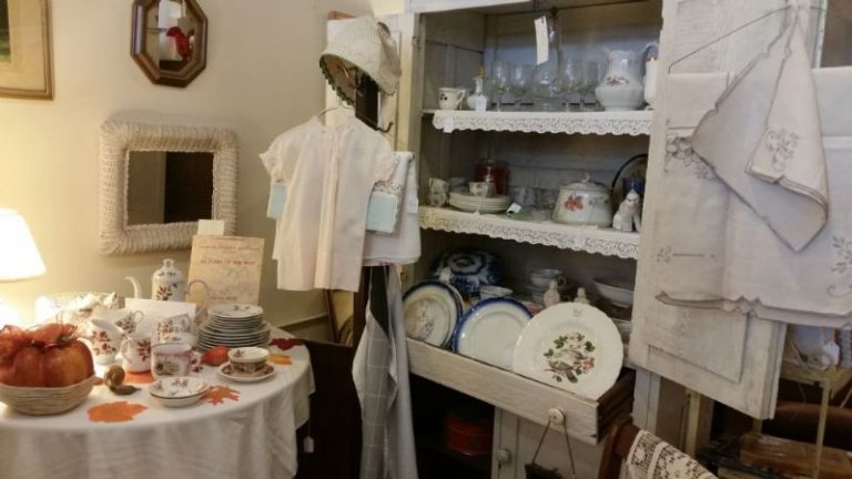 antique clothing on a coat tree, small table with dishes, and an old hutch filled with plates and glasses