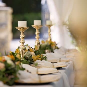 banquet table with gold candle holders, white pillar candles , china, floral arrangements and blurred out background