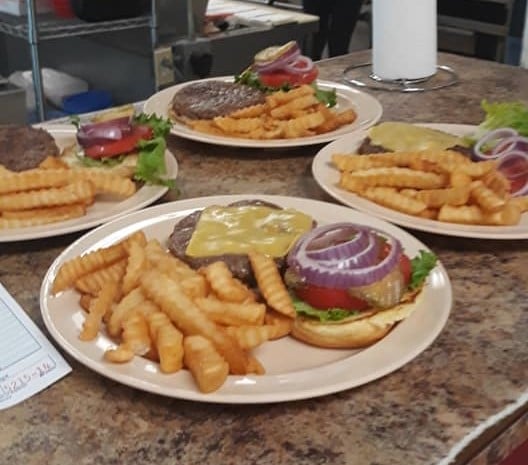 Four plates all with open faced cheese burgers and crinkle cut fries