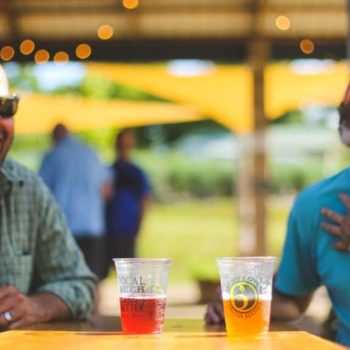 Two men laughing and drinking beer at West Sixth Farm